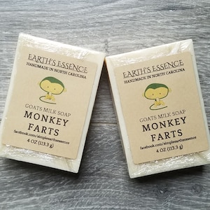 May include: Two bars of goat milk soap with a cartoon monkey design. The soap is labeled "EARTH'S ESSENCE" and "MONKEY FARTS". Each bar is 4 oz (113.3 g).