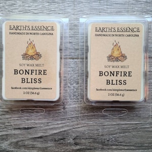 May include: Two 2 ounce soy wax melts in clear plastic containers. The labels are brown with a campfire illustration and the text "EARTH'S ESSENCE HANDMADE IN NORTH CAROLINA SOY WAX MELT BONFIRE BLISS facebook.com/simpleearthsessence 2 OZ (56.6 g)"