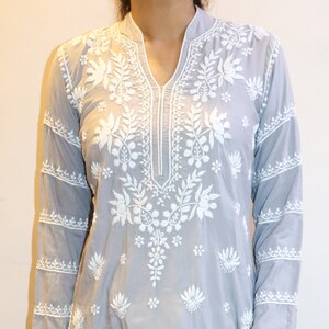 Puede incluir: Conjunto de kurta bordada gris claro y pantal&oacute;n blanco. La kurta presenta intrincados bordados florales blancos y mangas largas. El atuendo se combina con bailarinas de color rosa brillante. Ropa para uso casual o festivo.