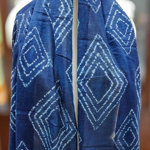 Peut inclure: Écharpe bleu foncé avec un motif de losanges blancs répétés. L'écharpe est faite d'un tissu léger et possède une bordure décorative. L'écharpe est drapée sur une forme, mettant en valeur son design.