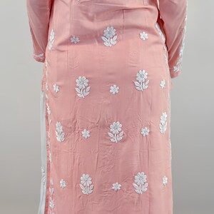 Puede incluir: Conjunto de t&uacute;nica rosa claro y pantal&oacute;n blanco con intrincados bordados florales blancos. La t&uacute;nica tiene mangas largas y cuello mandar&iacute;n. El pantal&oacute;n es holgado. El conjunto se usa con sandalias.