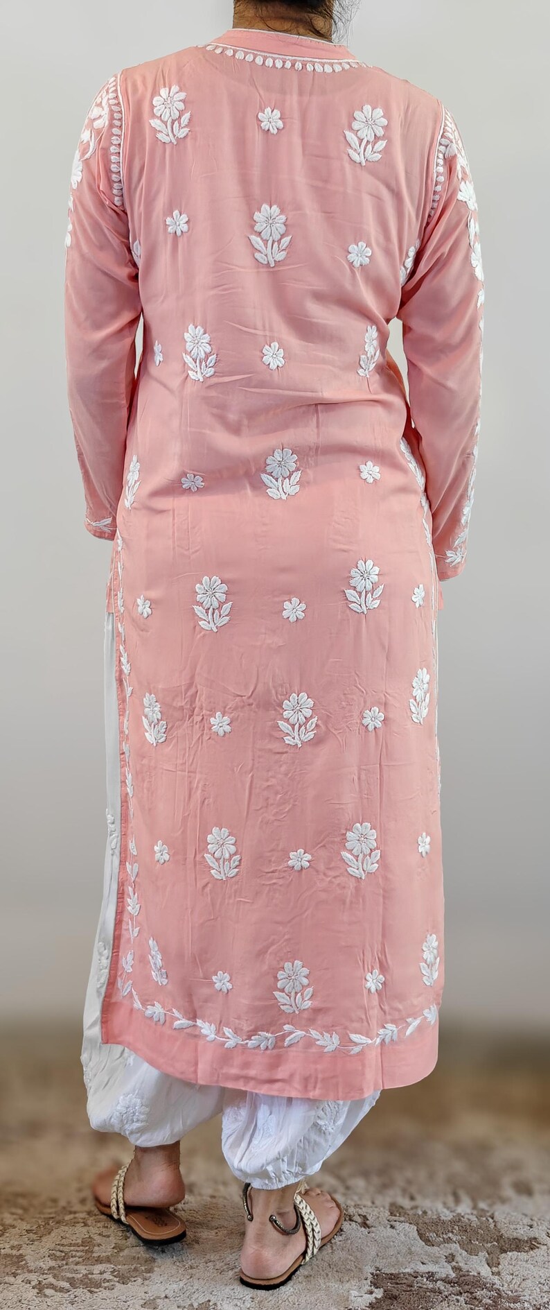Puede incluir: Conjunto de t&uacute;nica rosa claro y pantal&oacute;n blanco con intrincados bordados florales blancos. La t&uacute;nica tiene mangas largas y cuello mandar&iacute;n. El pantal&oacute;n es holgado. El conjunto se usa con sandalias.