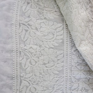 May include: White cotton fabric with a delicate floral embroidery pattern. The fabric is sheer and has a soft, flowing texture.