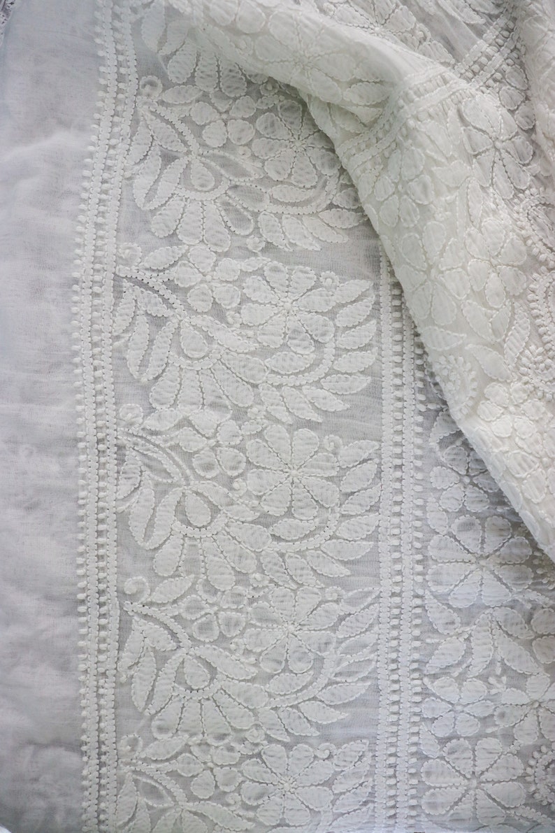May include: White cotton fabric with a delicate floral embroidery pattern. The fabric is sheer and has a soft, flowing texture.