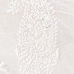 May include: Close-up of white fabric with intricate, raised embroidery. The design features a large paisley shape with floral and leaf details. The fabric has a slightly sheer quality, and the embroidery is densely packed.