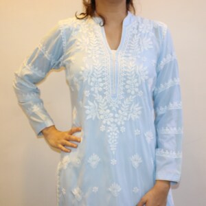 May include: A light blue tunic with long sleeves and intricate white floral embroidery. The tunic features a mandarin collar and a V-neckline. The embroidery is concentrated around the neckline and extends down the front, with additional detailing on the sleeves.