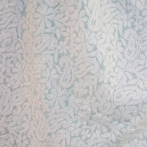 May include: White embroidered fabric with a delicate floral pattern on a light blue background.