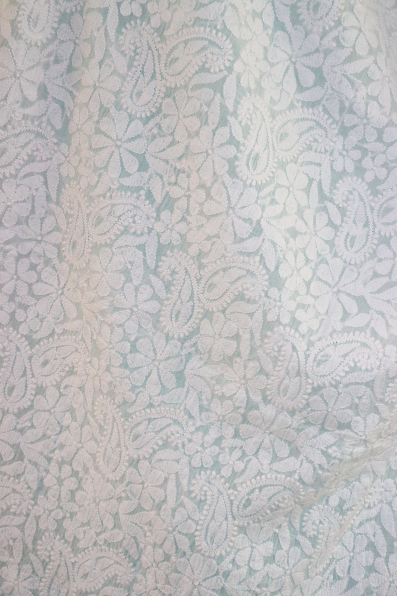 May include: White embroidered fabric with a delicate floral pattern on a light blue background.