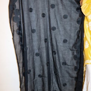 May include: A black sheer scarf with large, embroidered polka dots. The scarf is draped over a yellow and white floral patterned garment.