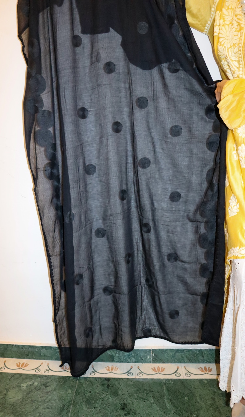 May include: A black sheer scarf with large, embroidered polka dots. The scarf is draped over a yellow and white floral patterned garment.