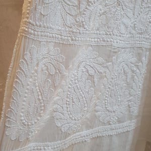 May include: White cotton fabric with intricate white embroidery featuring floral and paisley designs. The fabric has a delicate, sheer texture.