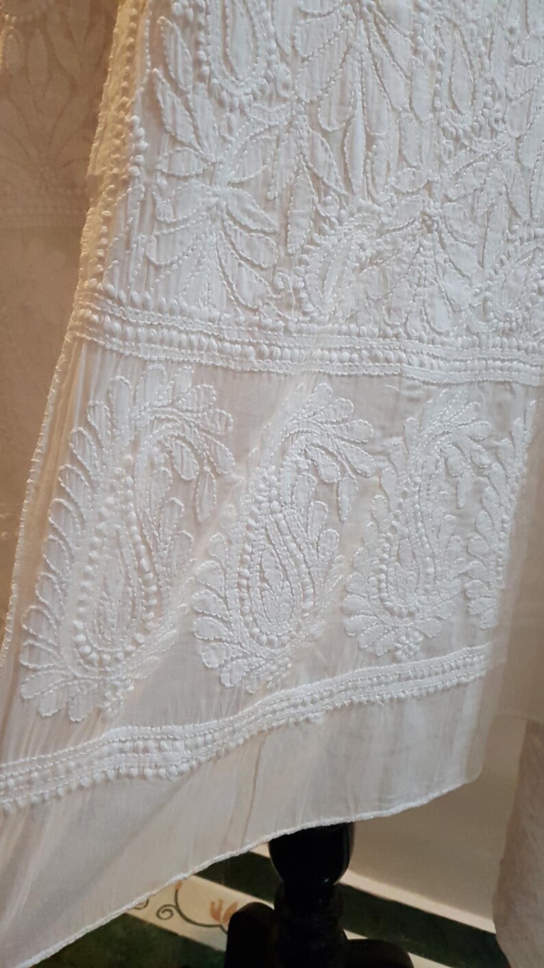May include: White cotton fabric with intricate white embroidery featuring floral and paisley designs. The fabric has a delicate, sheer texture.
