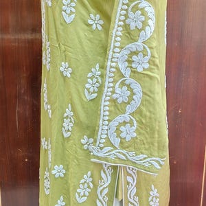 Puede incluir: Una t&uacute;nica verde claro con intrincados bordados florales blancos. La prenda de manga larga presenta patrones detallados a lo largo de las mangas y los bordes, con una abertura en el dobladillo. La t&uacute;nica se exhibe en un maniqu&iacute;.