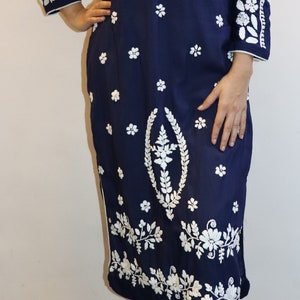 May include: Navy blue tunic dress with white floral embroidery. The long-sleeved dress features a mandarin collar and a split neckline. White floral embroidery adorns the sleeves, bodice, and hem. The dress is paired with white pants.