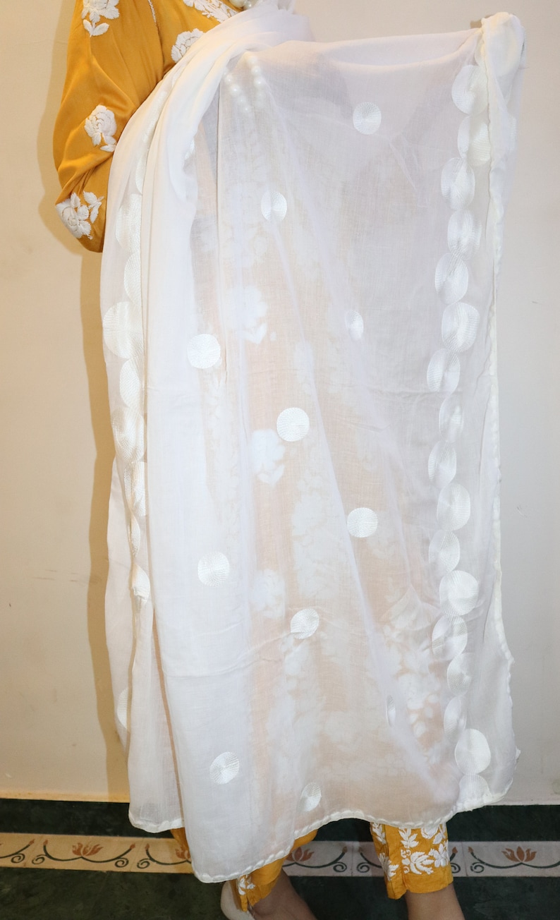 May include: White sheer scarf with embroidered white circles. The scarf is draped over a yellow and white outfit.