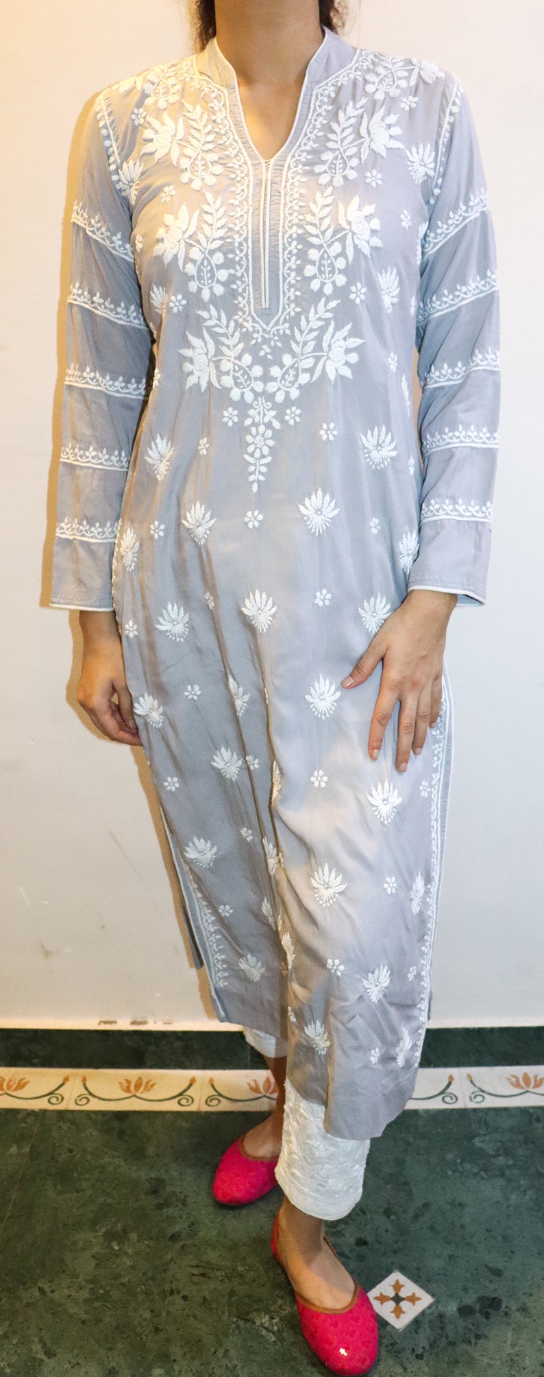 Puede incluir: Conjunto de kurta bordada gris claro y pantal&oacute;n blanco. La kurta presenta intrincados bordados florales blancos y mangas largas. El atuendo se combina con bailarinas de color rosa brillante. Ropa para uso casual o festivo.