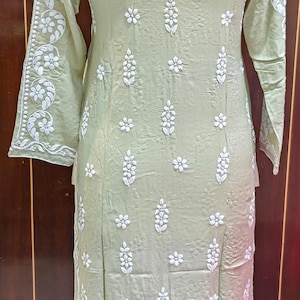 May include: A light green tunic dress with long sleeves and a mandarin collar. The dress is adorned with white floral embroidery. The embroidery is concentrated on the sleeves, front, and back of the dress. The dress is made of a lightweight fabric.