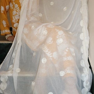 May include: White sheer scarf with embroidered white circles and floral designs. The scarf is draped over a yellow embroidered top.