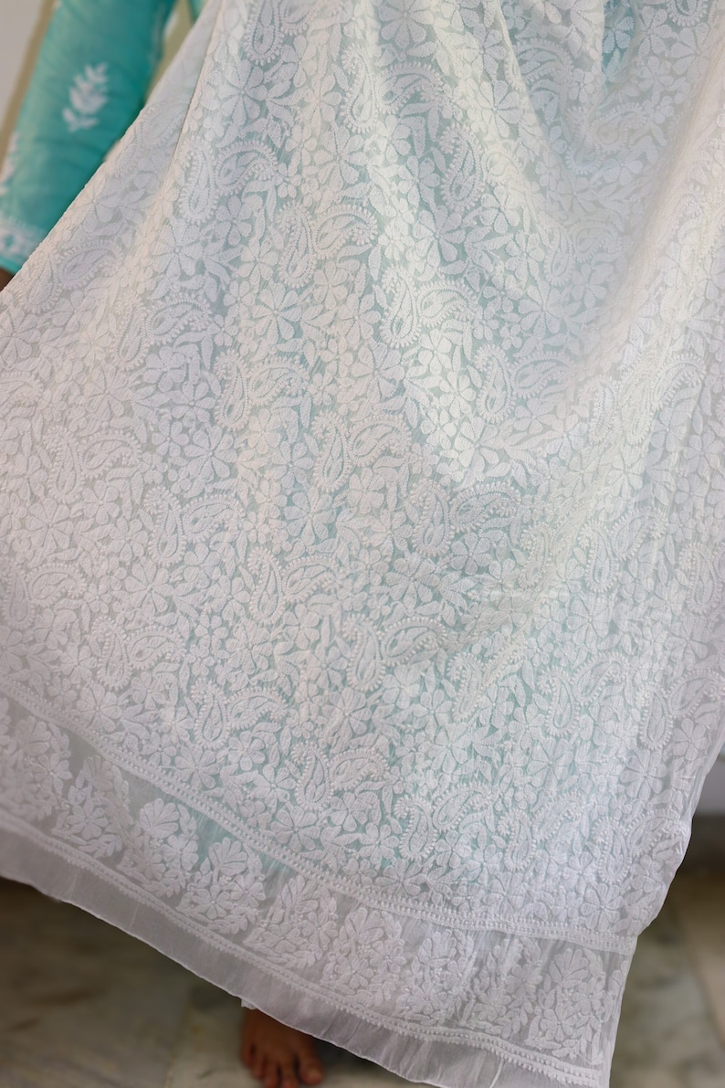 May include: White cotton fabric with a delicate floral embroidery pattern. The fabric is sheer and has a soft, flowing texture.