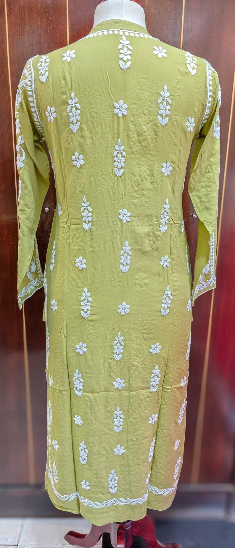 Puede incluir: Una t&uacute;nica verde claro con bordados florales blancos. La t&uacute;nica de manga larga presenta un cuello redondo y un corte recto. El bordado se concentra en la parte delantera y las mangas, con un motivo floral. La tela parece ser ligera.