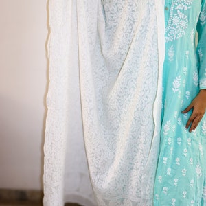 May include: A white embroidered sheer dupatta with a floral pattern. The dupatta is draped over a turquoise blue dress with white embroidery.