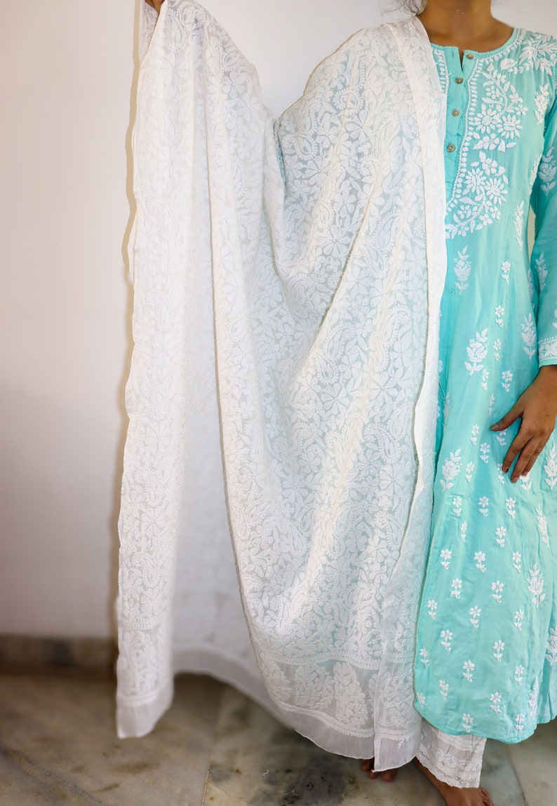 May include: A white embroidered sheer dupatta with a floral pattern. The dupatta is draped over a turquoise blue dress with white embroidery.