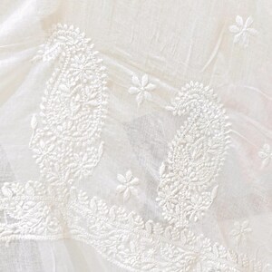 May include: White fabric with intricate embroidered paisley and floral designs. The fabric has a delicate, sheer quality, with a tasseled edge. The embroidery is detailed and adds texture to the textile.