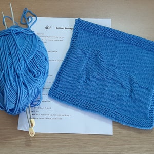 May include: Knitting pattern for a blue cotton dishcloth with a dog design. The pattern includes instructions for knitting the dishcloth and a ball of blue yarn.
