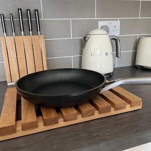 May include: A black frying pan with a silver handle sits on a wooden slatted trivet. A white kettle and a white toaster with the word "SMEG" on it are in the background.