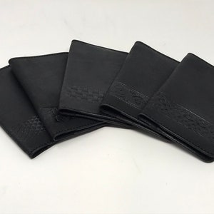 May include: Five black rectangular passport holders arranged in a fan shape. Each holder features a distinct embossed pattern along the bottom edge, including geometric, woven, and intricate knotwork designs on a smooth, matte black surface.