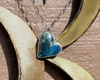 Può includere: Una collana con catena d'argento con un ciondolo a forma di cuore. Il ciondolo è fatto di una pietra blu e verde con un motivo a spirale.
