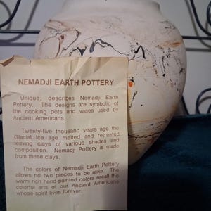 May include: A handcrafted Nemadji Earth Pottery vase with a unique design. The off-white vase features brown and black marbling. A tag describes the pottery's origins and the symbolism of the designs.