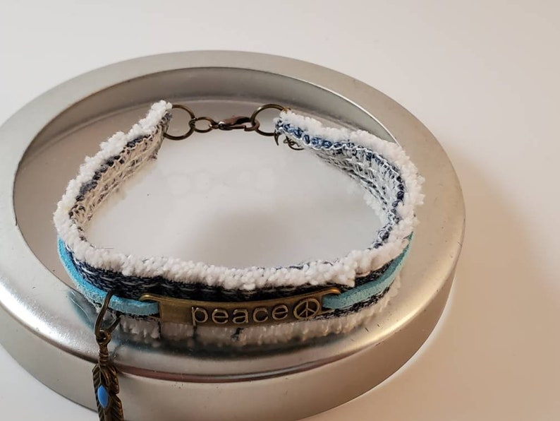 Fringed blue denim bracelet with bronze PEACE center and feather charm with aqua stone
