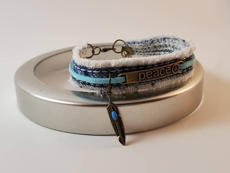 Fringed blue denim bracelet with bronze PEACE center and feather charm with aqua stone