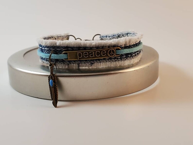 Fringed blue denim bracelet with bronze PEACE center and feather charm with aqua stone