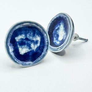 May include: Two ceramic cabinet knobs with a blue and white design. The knobs have a round shape with a dark blue center and a lighter blue border. The white design in the center resembles a cracked pattern. Each knob has a silver screw for installation.
