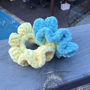 Könnte beinhalten: Zwei flauschige Haargummis sind abgebildet. Eines ist ein weiches Gelb, das andere ein Farbverlauf aus Blau und Gelb. Diese handgefertigten Haaraccessoires sind perfekt, um jeder Frisur einen Hauch von Farbe und Textur zu verleihen.