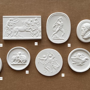 May include: A collection of nine white plaster relief plaques featuring classical motifs, including figures, chariots, and portraits. Each piece is numbered from 1 to 9, displaying intricate raised designs on various geometric shapes like circles and rectangles.