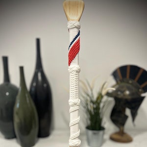 May include: A wooden paddle with a white rope handle. The rope is wrapped in a diagonal pattern with red, white, and blue stripes. The paddle is about 30 inches long.