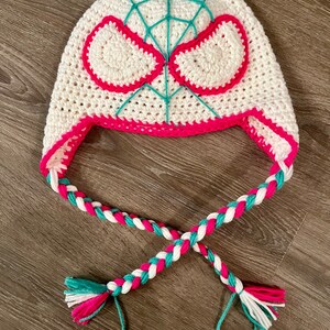 May include: White crocheted hat with a pink and teal spider web design and matching braided ties.
