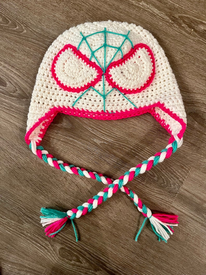 May include: White crocheted hat with a pink and teal spider web design and matching braided ties.