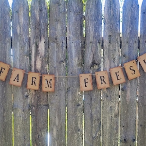 May include: A brown paper banner with the words "FARM FRESH" strung on a twine line against a wooden fence.