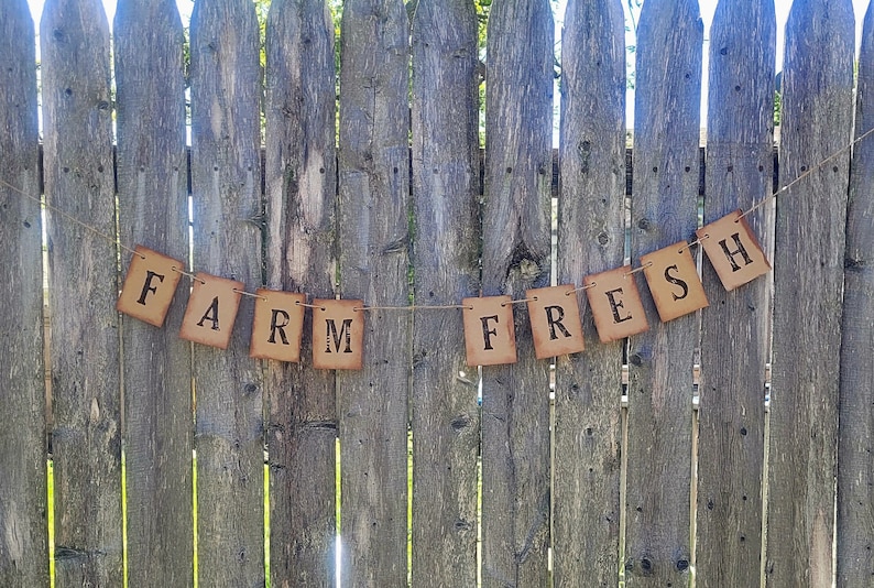 May include: A brown paper banner with the words "FARM FRESH" strung on a twine line against a wooden fence.