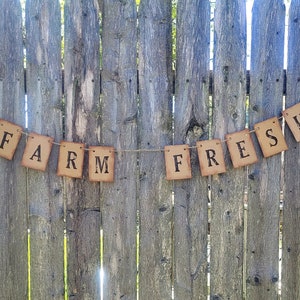 May include: A rustic brown paper banner with the words "FARM FRESH" strung on twine against a weathered wooden fence.