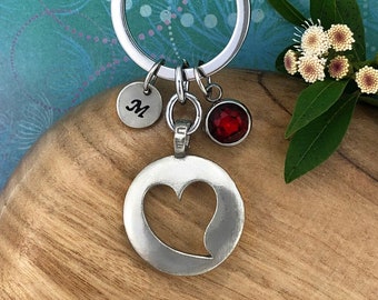 May include: A silver keychain with a heart-shaped cutout, a red rhinestone charm, and a silver charm with the letter "M" engraved on it.