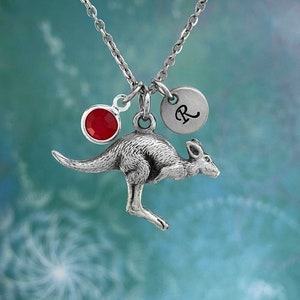 May include: A silver kangaroo charm necklace with a red crystal and a silver charm with the letter 'R' on it.