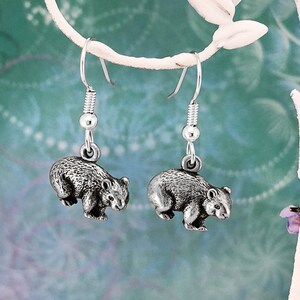 May include: Silver dangle earrings featuring a detailed 3D wombat charm. The earrings are hanging from a silver hook.