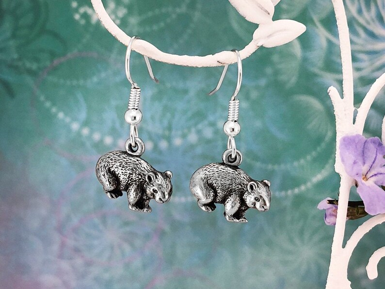 May include: Silver dangle earrings featuring a detailed 3D wombat charm. The earrings are hanging from a silver hook.