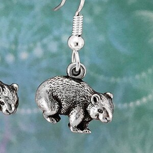 May include: Silver dangle earrings featuring a detailed miniature wombat charm. The earrings have a silver hook fastening.