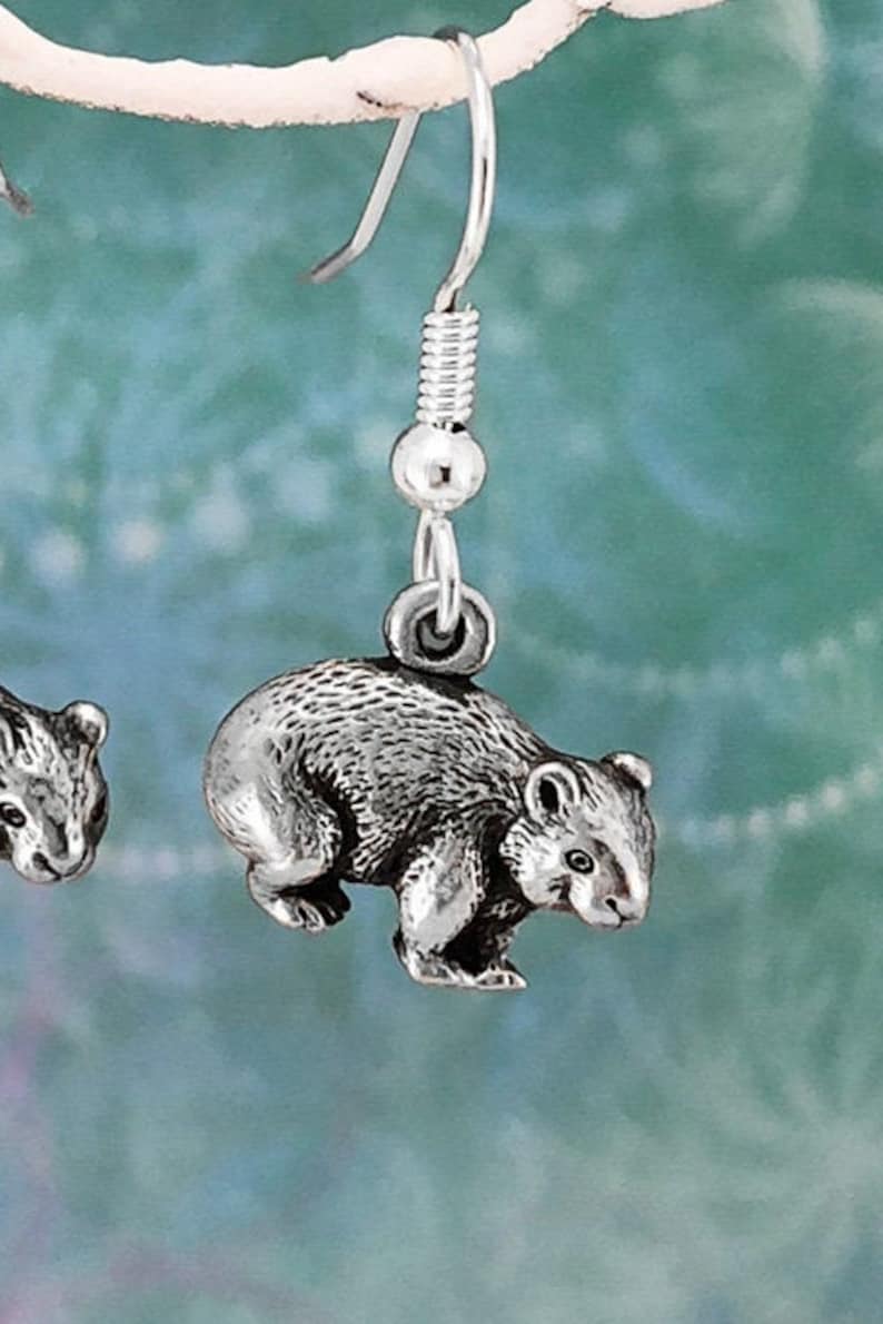 May include: Silver dangle earrings featuring a detailed miniature wombat charm. The earrings have a silver hook fastening.